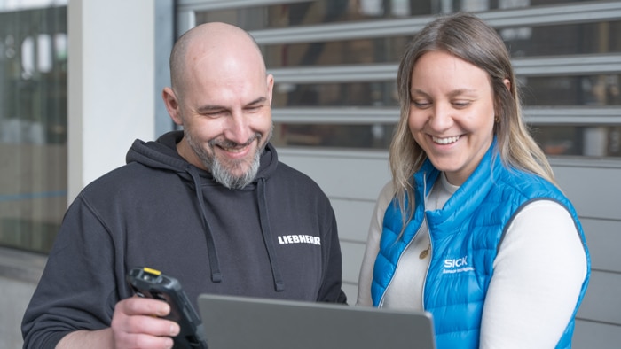 Liebherr employee scans goods data with a handheld device while reviewing incoming goods information on a laptop together with a SICK representative