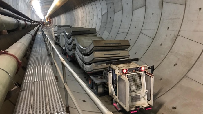 Vehicle transporting concrete segments through a tunnel with concrete lining.
