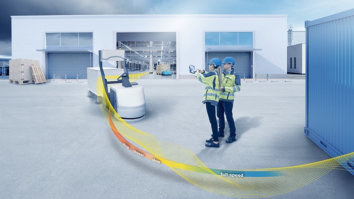 A man with a tablet kneels in the outside area of a plant.